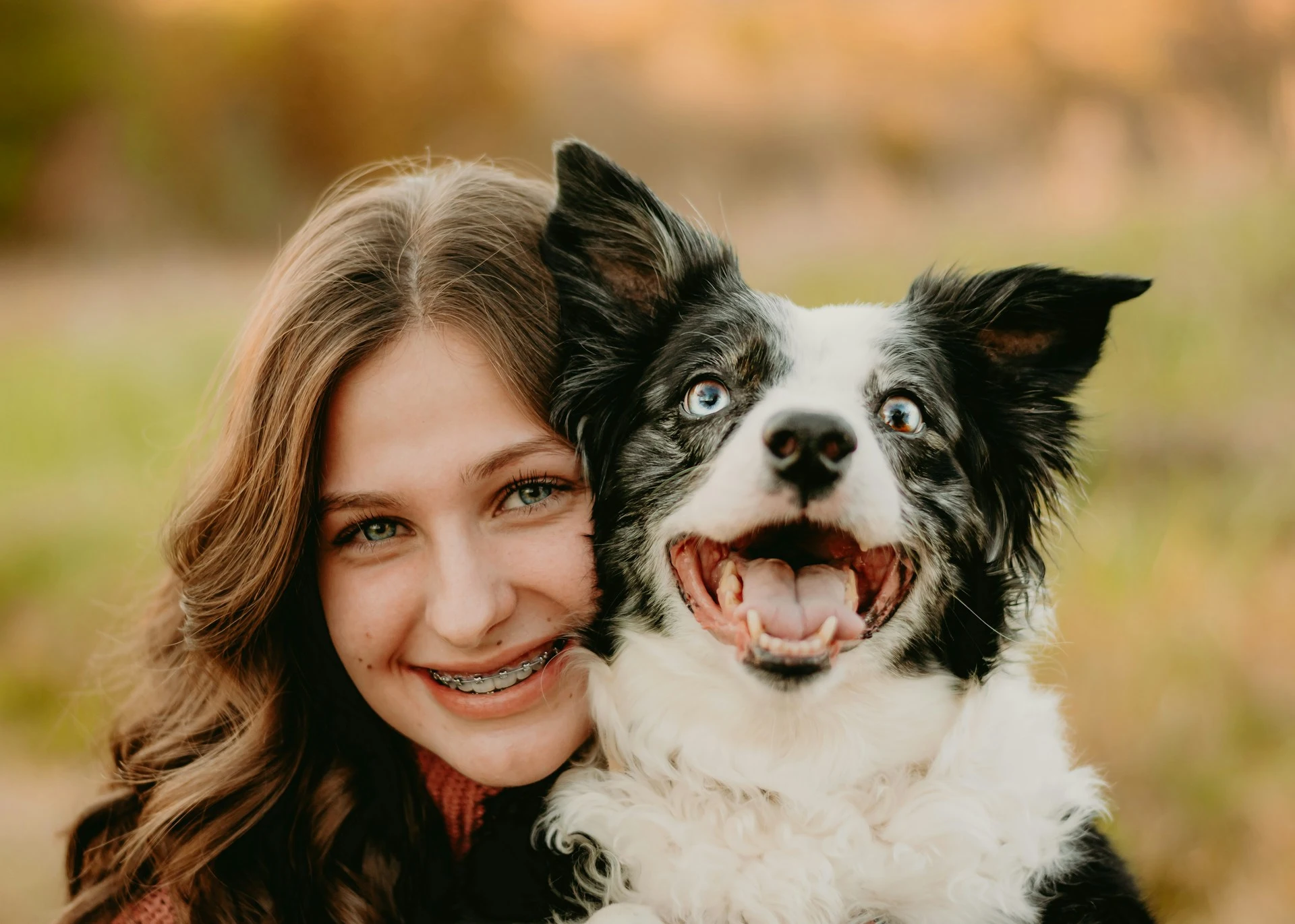 A girl with braces is smiling while cuddling up to a large, smiling Border Collie.